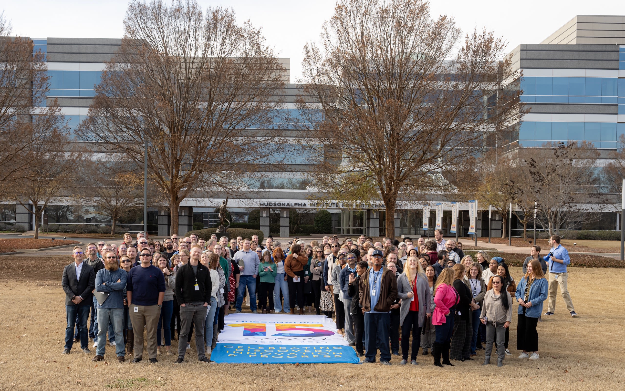 A large group of people gathered around a banner that says 'HudsonAlpha 15th Anniversary' 