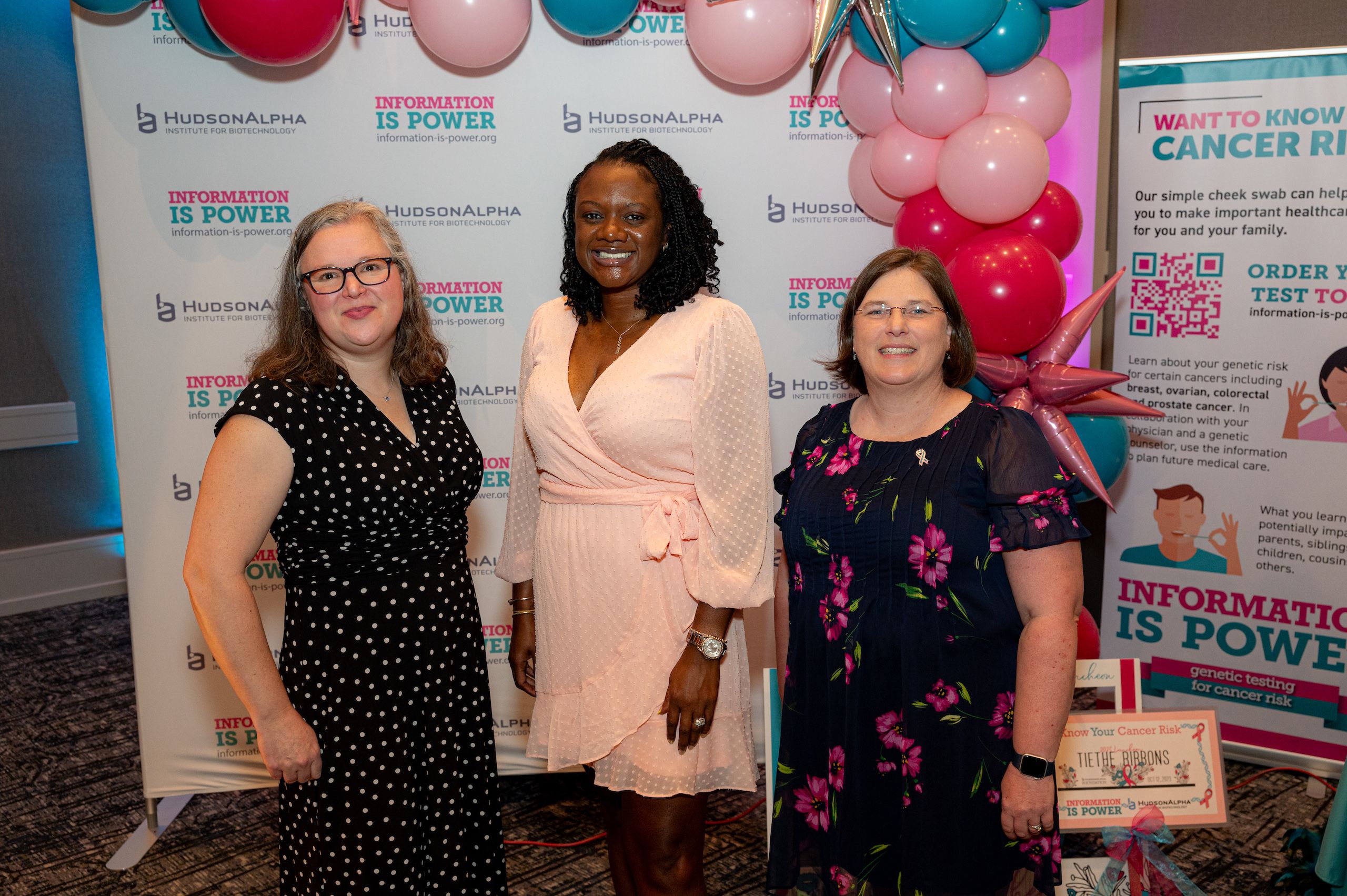 Three women standing in front of a pink and turquoise balloon arch