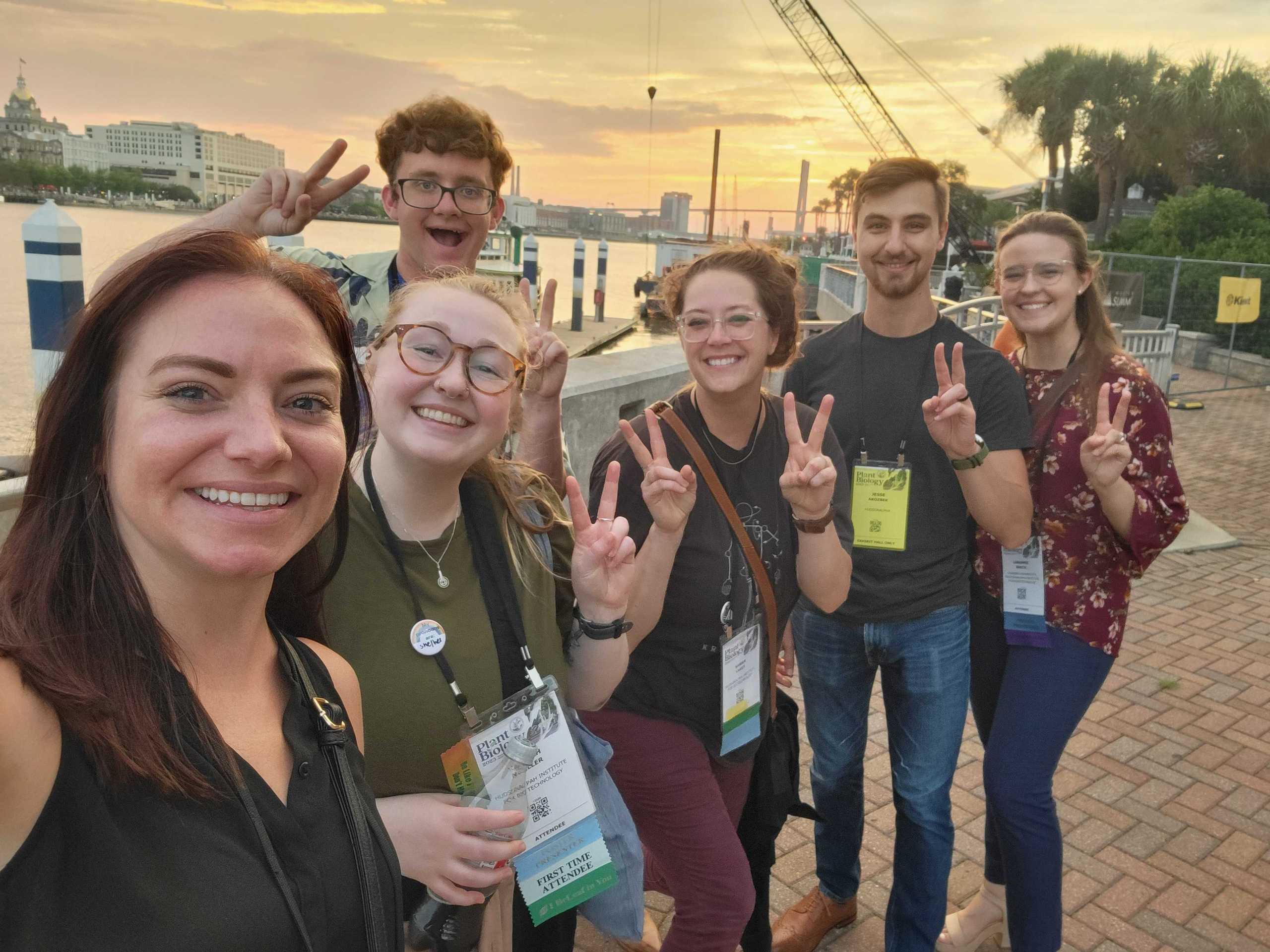 A group of young people holding up peace signs in front of a harbor