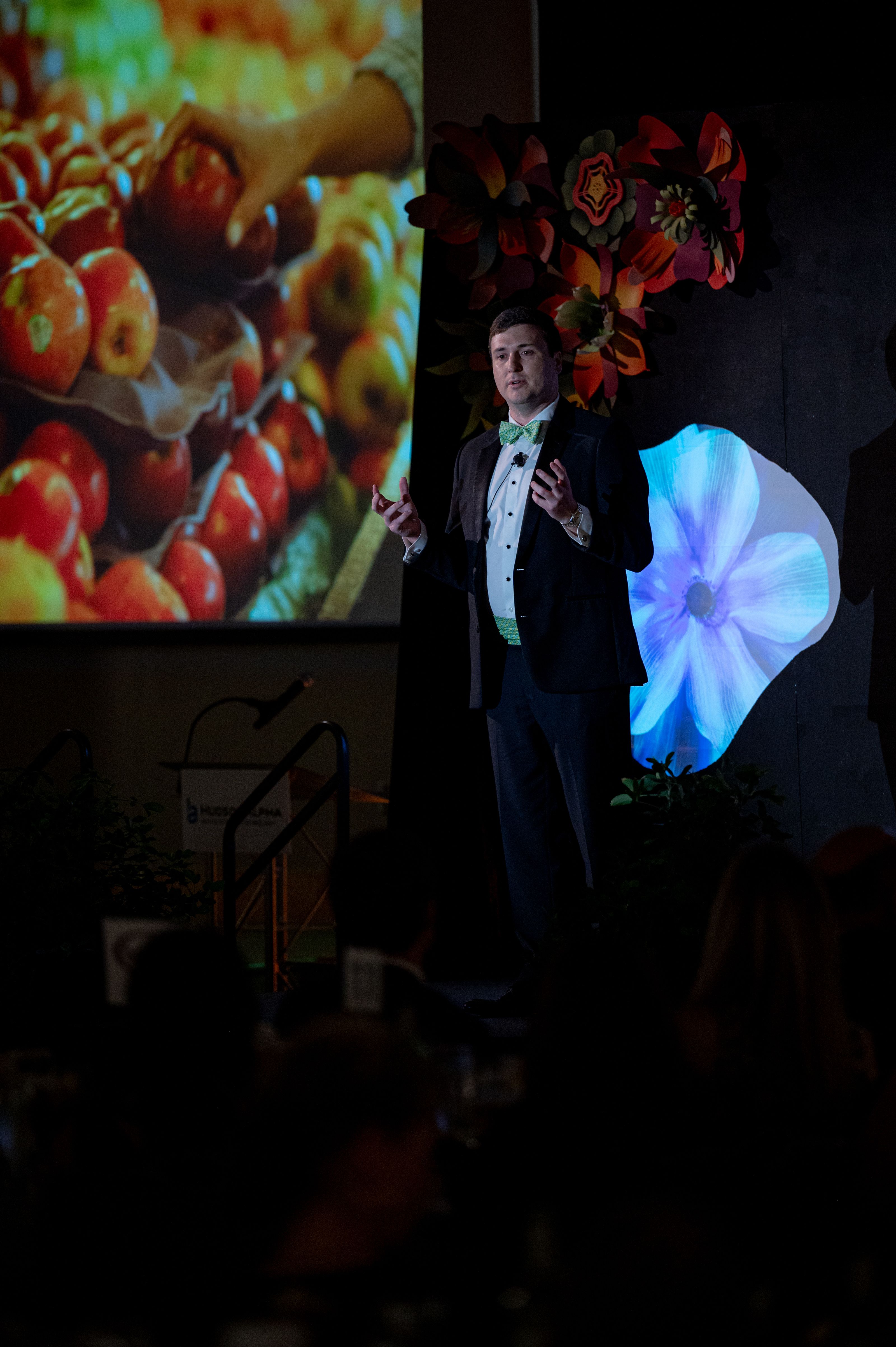 A man in a tuxedo presenting in front of a screen with vivid colors