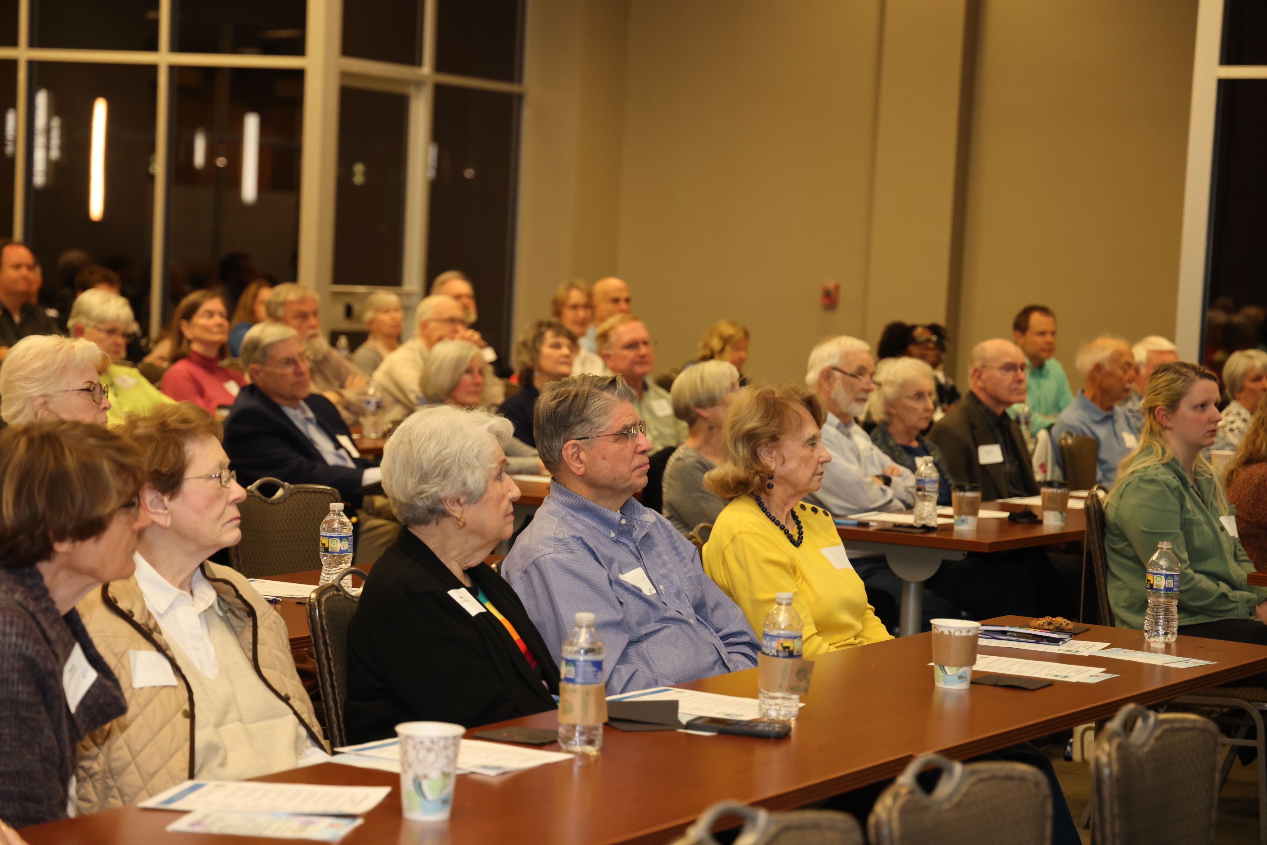 Multiple people listening intently to a talk. These people are sitting at a long table.